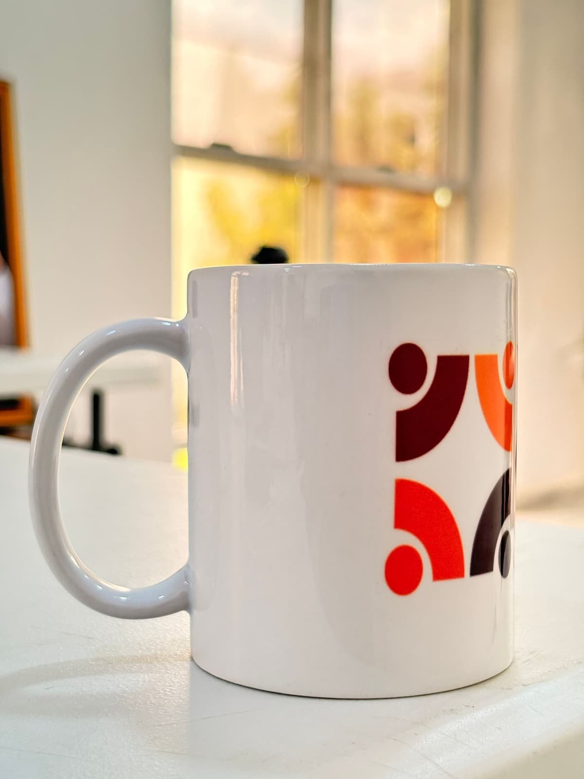 Taza de cerámica blanca con diseño impreso a todo color junto a una ventana