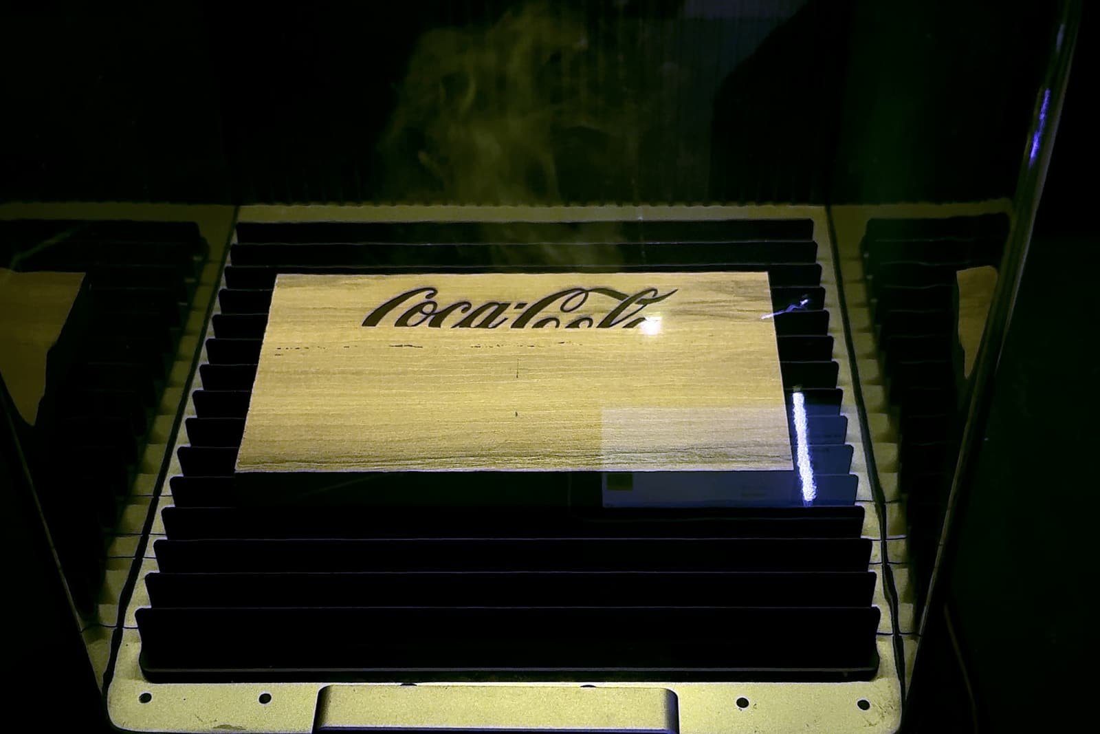 Grabado láser sobre una placa de madera dentro de la máquina, con el humo del corte subiendo